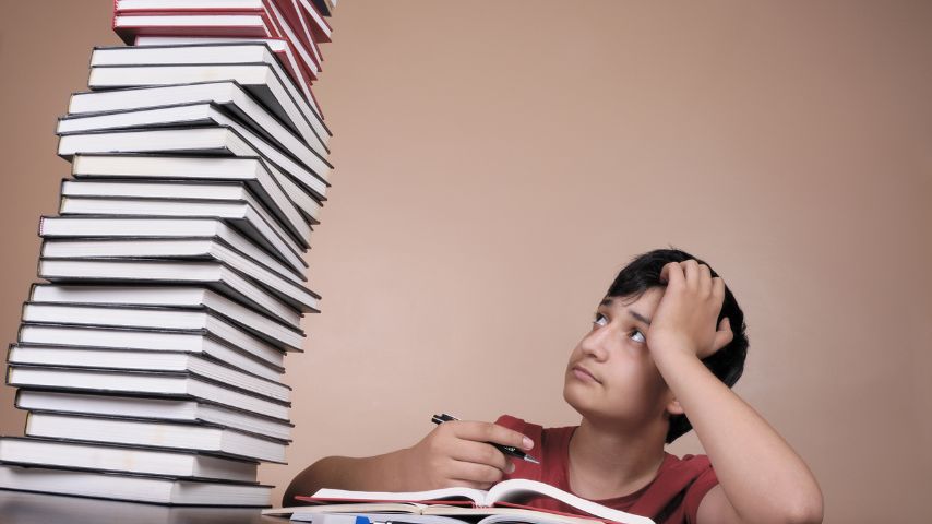 Młody chłopiec, nad którym jest stos książek, zastanawia się, jak zmotywować się do nauki.